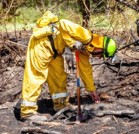 A firefighter in full PPE feeling for heat in burnt ground with a bare hand
